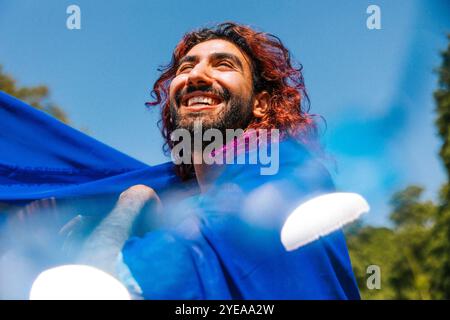 Vista dall'angolo basso dell'uomo felice con i capelli tinti ricoperti di dupatta blu sotto il cielo Foto Stock