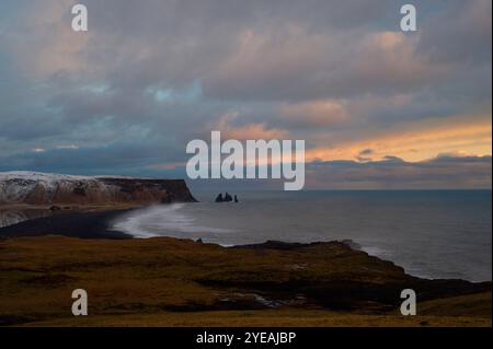 Vista spettacolare del cielo mooso e delle onde che si infrangono sulla spiaggia di sabbia nera di Reynisfjara al tramonto; spiaggia di sabbia nera di Reynisfjara, Dyrhólaey, Islanda Foto Stock