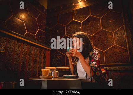 Yerevan, Armenia - 19 ottobre 2024: Donna turistica gusta un drink di caffè fresco cappuccino nel caffè Lumen Coffee 1936. Speciale, famoso, vecchio ed elegante caffè Foto Stock