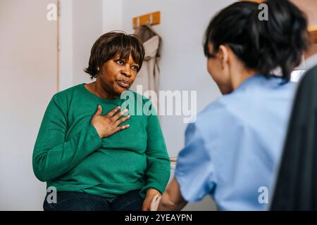 Donna anziana con la mano sul petto che parla con un medico mentre è seduta nella sala esame Foto Stock