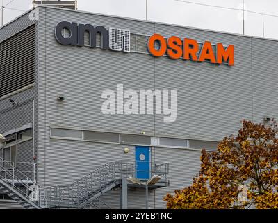 Unternehmen a Ratisbona Das Werk der Osram Opto Semiconductors GmbH, Teil der ams Osram AG, a Ratisbona. Auf der Metallfassade des Gebäudes befindet sich das Firmenlogo ams OSRAM in schwarzen und orangefarbenen Buchstaben. Eine blaue Zugangstür und eine Außentreppe sind ebenfalls sichtbar. Regensburg Burgweinting - Harting Bayern Deutschland *** azienda a Ratisbona lo stabilimento di Osram Opto Semiconductors GmbH, parte di ams Osram AG, a Ratisbona il logo aziendale ams OSRAM in lettere nere e arancioni è visibile sulla facciata metallica dell'edificio Una porta di accesso blu e una scala esterna Foto Stock