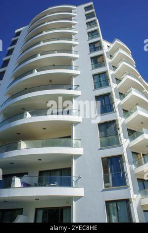 Un alto e suggestivo edificio presenta un'architettura contemporanea con eleganti curve e balconi in vetro in una giornata di sole. Foto Stock