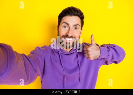 Foto ritratto di un giovane uomo scattate un selfie con il pollice su un elegante abito viola isolato su sfondo giallo Foto Stock