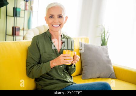 Foto dell'adorabile dolce signora indossa una camicia kaki bevendo un caffè caldo e gustoso all'interno della casa Foto Stock