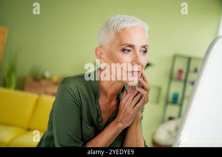 Foto di signora piuttosto preoccupata indossare camicia verde che guarda specchio pelle interno stanza casa casa Foto Stock