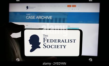 Persona che tiene un cellulare con il logo dell'organizzazione legale statunitense Federalist Society sullo schermo davanti alla pagina web. Mettere a fuoco il display del telefono. Foto Stock