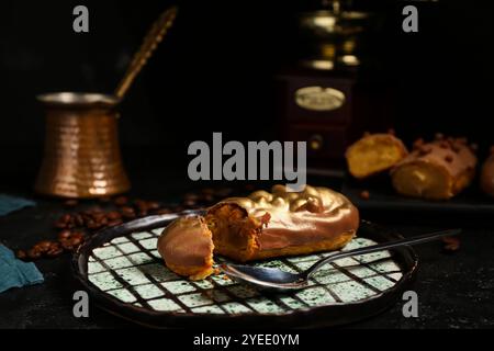 Piatto con eclair dolce e chicchi di caffè su sfondo scuro Foto Stock