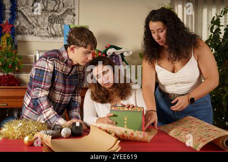 Tre persone sono riunite intorno a un tavolo, una di loro guarda una scatola verde. La scena è spensierata e festosa, come probabilmente il gruppo si sta preparando Foto Stock