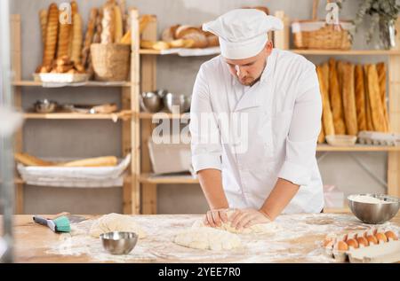 il fornaio professionista si trova al banco di lavoro, impastando e modellando l'impasto per preparare pane e baguette Foto Stock