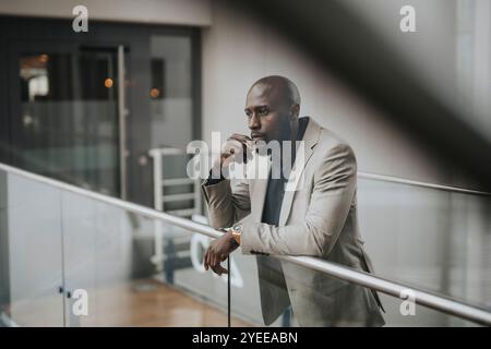 Un uomo d'affari calvo e premuroso appoggiato a una ringhiera di vetro Foto Stock
