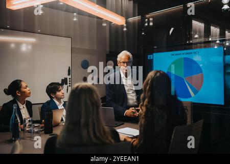 Uomo d'affari anziano che discute i piani con colleghi di sesso maschile e femminile in sala riunioni Foto Stock