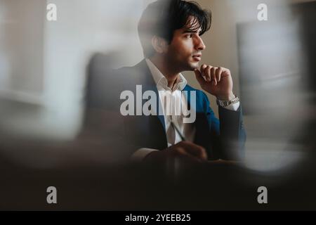 Giovane uomo d'affari seduto con la mano sul mento in ufficio Foto Stock