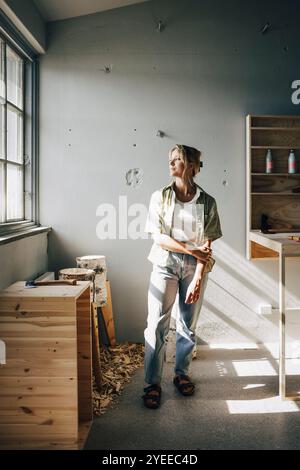 Imprenditrice donna premurosa che guarda attraverso la finestra dell'officina Foto Stock