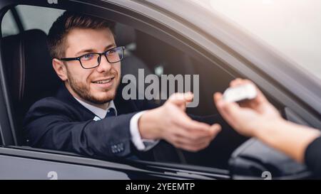 Giovane uomo portatore che prende la chiave automatica, seduto sul sedile del conducente Foto Stock