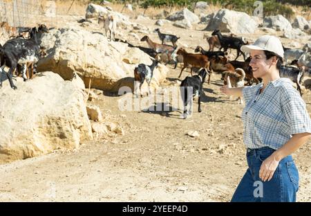 Felice successo latino femmina prendere capre per camminare sulla zona rocciosa vicino a casa colonica Foto Stock