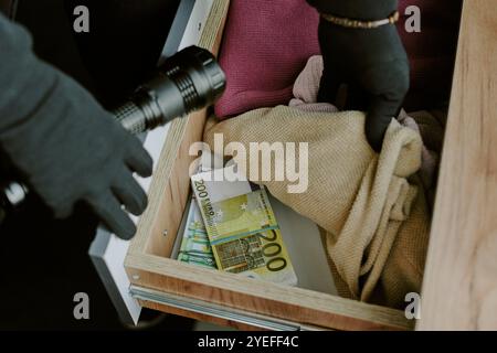 Scatto ad angolo alto di un ladro irriconoscibile che passa attraverso il comò con vestiti e un sacco di soldi Foto Stock