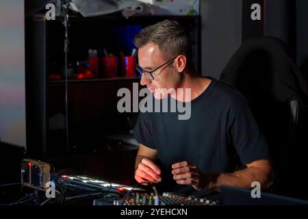 Tecnico audio specializzato che utilizza una console di missaggio audio professionale in un ambiente da studio poco illuminato Foto Stock