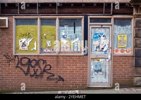 Un magazzino abbandonato e vuoto a Sheffield, in Inghilterra. Il negozio, raffigurato nel 2024 e in precedenza un parrucchiere, fu occupato l'ultima volta intorno al 2016. Le finestre sono state sbiancate, con vecchi poster e alcuni graffiti visibili. Foto Stock