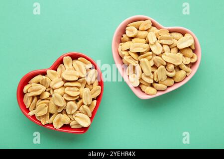 Arachidi in una ciotola a forma di cuore su sfondo di menta. Vista dall'alto Foto Stock