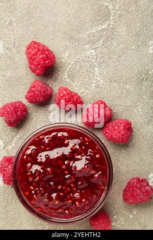 Marmellata di lamponi nel recipiente con frutti di bosco su sfondo grigio di cemento. Foto verticale Foto Stock