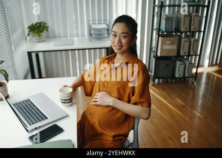 Ritratto di donna incinta che beve caffè in ufficio Foto Stock