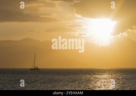 Una barca a vela su un mare calmo al tramonto con un cielo dorato e montagne sullo sfondo, Agia Kyriaki, Nafplio, Nauplia, Nauplion, Nauplia, Argolis, Arg Foto Stock