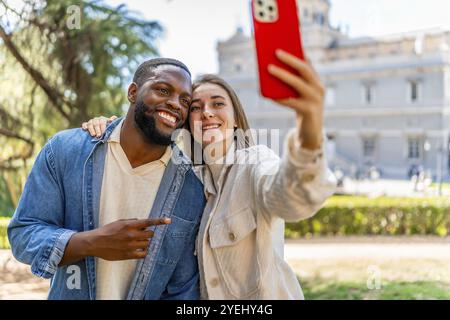 Felice coppia multietnica che scatta selfie e sorride in un parco con vista sulla città Foto Stock