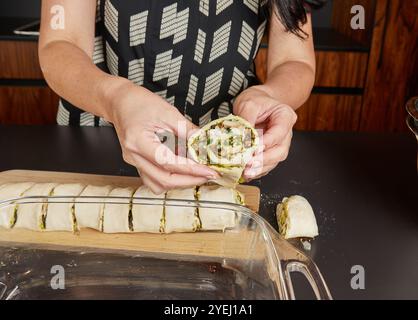 Una persona tiene un rotolo a fette pieno di pesto, funghi e formaggio, rivelando il ricco ripieno e gli strati all'interno. Foto Stock