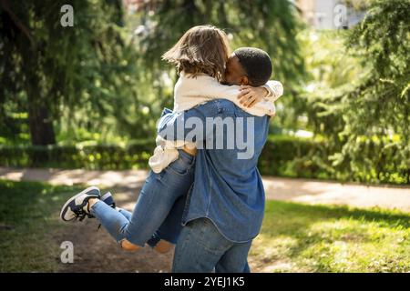 Coppia multietnica innamorata che abbraccia e salta insieme in un parco Foto Stock