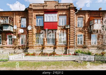 Edificio storico in mattoni con recinzione bianca per picchetti e giardino di tulipani. La facciata di un vecchio edificio in mattoni con finestre, decorata con una recinzione bianca e un Foto Stock