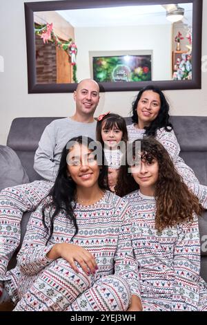 Una famiglia allegra, vestita con pigiama di Natale abbinato, posa sul divano, godendosi le vacanze in una casa festiva. Foto Stock