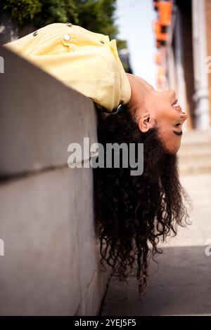 Foto di una giovane ragazza positiva con una studentessa di capelli ondulati in un'elegante giacca gialla che trascorre del tempo all'aperto rilassandosi a terra Foto Stock