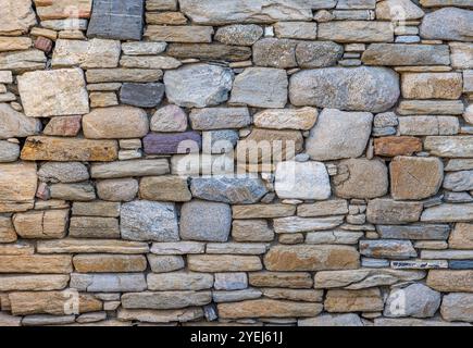 Sfondo strutturato e senza cuciture di un antico muro di pietra con pietre di forma e dimensioni diverse Foto Stock