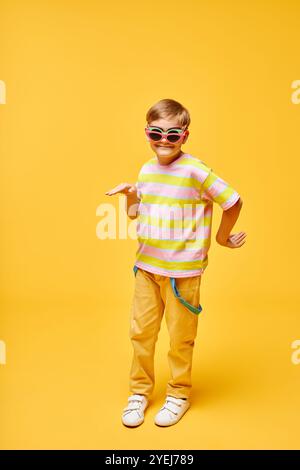 Ripresa verticale di un preadolescente sorridente che si inganna mentre balla con tre paia di occhiali da sole colorati su sfondo giallo in studio, copia spazio Foto Stock