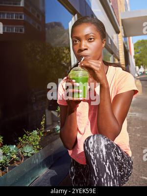 Donna nera, fitness e bere con frullato in città per idratazione, disintossicazione o salute e benessere. Giovane africano, donna o succo biologico per Foto Stock