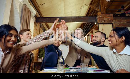 Membri di team di diverse origini che danno un punteggio di cinque, celebrando i risultati raggiunti e la potenza della collaborazione Foto Stock