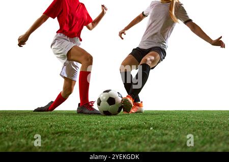 Immagine ritagliata di calciatrici in movimento sullo stadio, dribbling ball, allenamento su sfondo bianco. Concentrati sulle gambe. Foto Stock