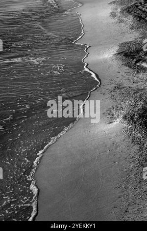 Onde mattutine su Sandy Beach: Contrasto superficiale bagnato e asciutto sulla costa. Bianco e nero. Grecia 2024 Foto Stock