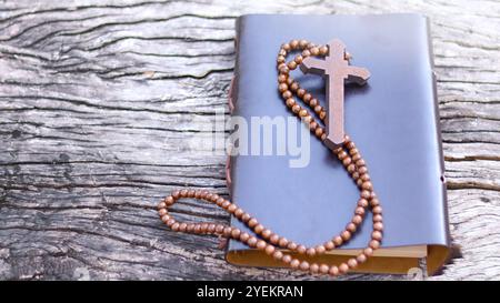 Croce di legno rosso scuro su una copertina di libri su sfondo di legno che simboleggia la diffusione dell'amore di Gesù Cristo tra i cristiani che riflette la fede la devozione e la fede Foto Stock