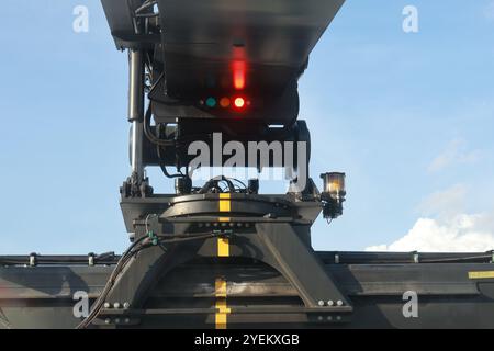 Primo piano di un impilatore a scorrimento carico che solleva un contenitore, mettendo in evidenza il braccio del macchinario e il meccanismo di sollevamento contro un cielo blu chiaro. Foto Stock