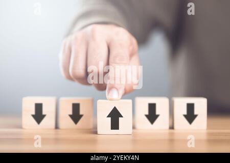 Uomo che seleziona un simbolo di freccia su blocchi di legno, simboleggia il concetto di pensare in direzioni diverse ed esplora prospettive alternative in Foto Stock