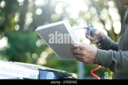 Il proprietario di un'auto è in possesso di un filtro dell'aria per l'esame. L'importanza dell'ispezione, della pulizia e della sostituzione regolari dei filtri dell'aria dell'auto sottolinea la manutenzione Foto Stock