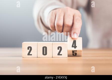 Hand sostituisce "2024" con "2025" utilizzando blocchi numerici, simboleggiando la transizione verso il nuovo anno, rappresentando il cambiamento, il progresso e i PA in corso Foto Stock