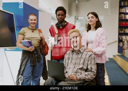 Ritratto di un gruppo di studenti multietnici sorridenti mentre guardano la fotocamera in una moderna libreria, che mostra vari stili e tiene in mano libri e laptop Foto Stock