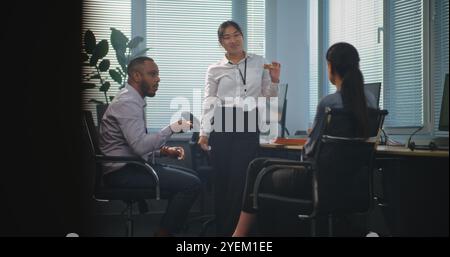 Un team di diversi dipendenti aziendali parla e mangia la pizza a domicilio per pranzo. Gruppo di operatori del supporto tecnico che hanno avuto una pausa dal lavoro in un moderno e luminoso ufficio di call center dotato di computer. Foto Stock