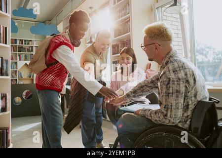 Gruppo di studenti che collaborano nella biblioteca scolastica con la luce del sole che scorre attraverso la finestra, creando un'atmosfera inclusiva e di supporto per l'apprendimento Foto Stock