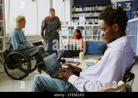 Membri di team di varie origini in un ambiente d'ufficio vivace e moderno, che collaborano a progetti. Scaffali, computer portatili e posti a sedere casual creano un ambiente coinvolgente per la discussione Foto Stock