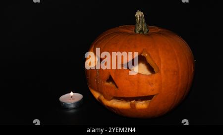 Jack-o-lantern che guarda il tealight su uno sfondo nero Foto Stock