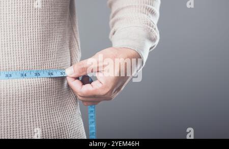 Primo piano di qualcuno che usa un metro blu per misurare la vita o i fianchi, simboleggiando il concetto di mantenere un corpo sano e prevenire Foto Stock