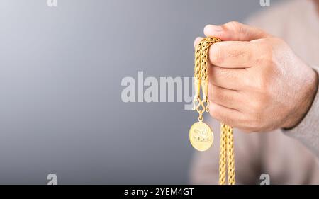 Primo piano di un uomo che tiene in mano una collana d'oro, che simboleggia il concetto di valore del mercato dell'oro. Riflette controllando l'autenticità dell'oro, e Foto Stock